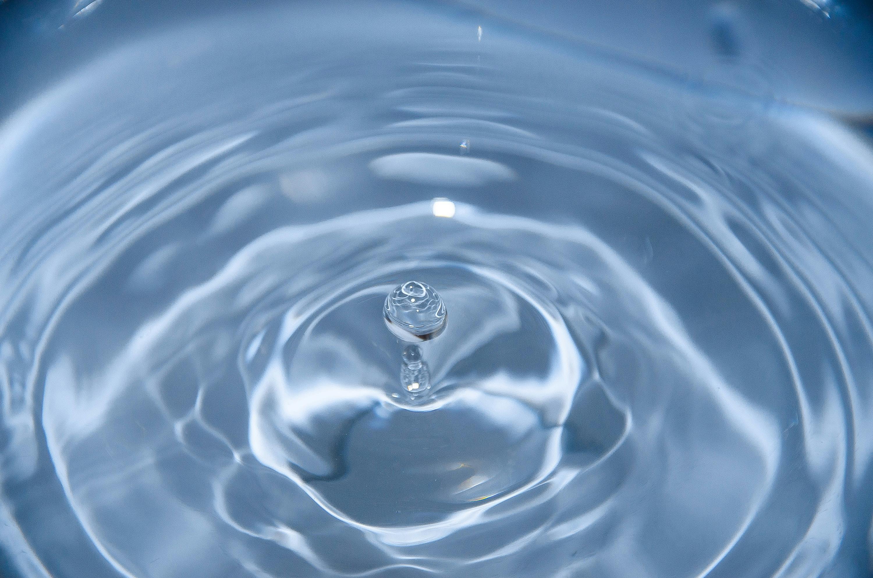 Gota de agua limpia y cristalina generando salpicaduras y ondas en la superficie.