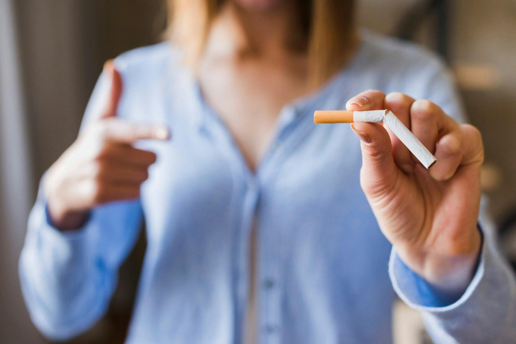 Primer plano de la mano de una mujer sosteniendo un cigarrillo partido a la mitad, haciendo alución a dejar el mal hábito de fumar.