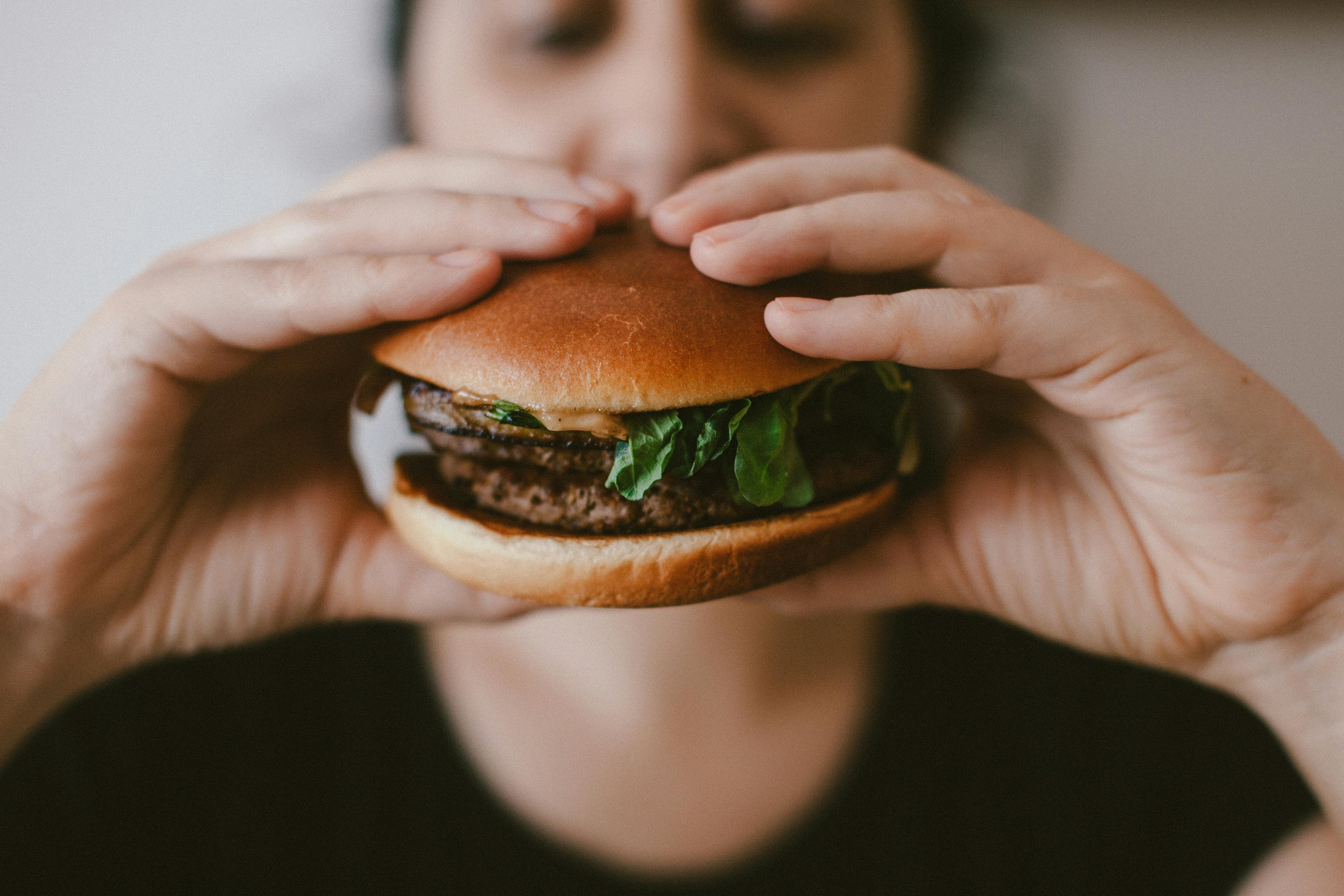Dos manos de una mujer adulta sosteniendo una hamburguesa que está a punto de comerse